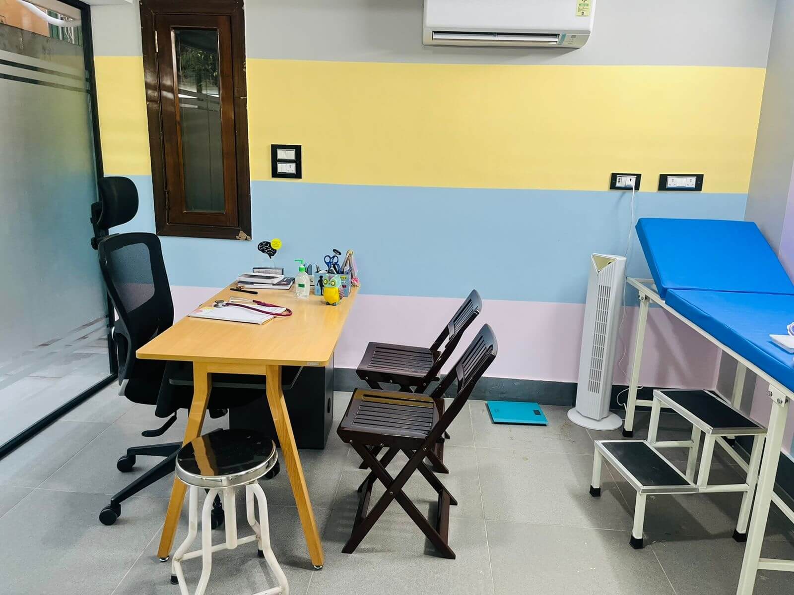 Dr. Bansal's consulting room at Magical Minds, with her desk, chairs for parents and an examination couch with a step